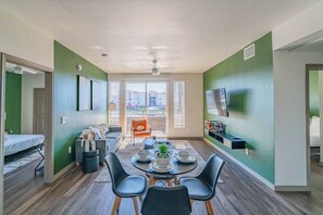 A modern living room with a dining area, a sofa, a coffee table, and a TV mounted on the wall.