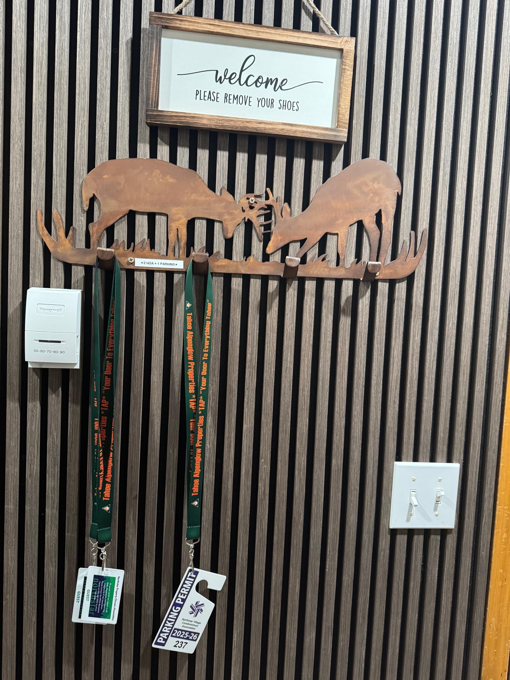 A wooden wall with a welcome sign, two moose antlers, and lanyards with ID badges.