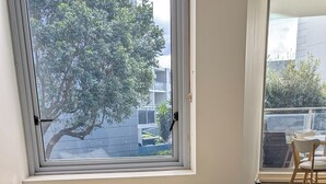 Een hoekbureau met een stoel, een raam met uitzicht op gebouwen en bomen, en een vloerbedekking.