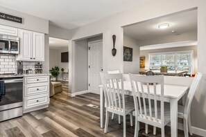 Una cocina moderna con armarios blancos, horno integrado y un comedor con sillas y mesa blancos.