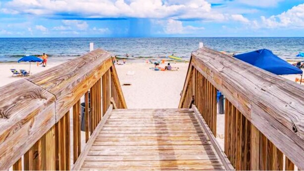 Eine Holzstege zu einem Strand mit Sonnenschirmen und Menschen.
