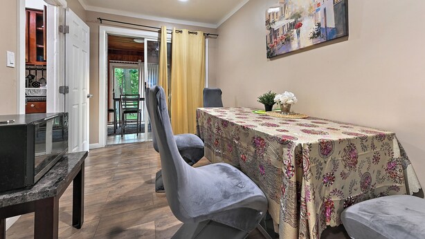 Un comedor con una mesa cubierta con mantel floral, dos sillas tapizadas de color gris y un ventilador de techo.