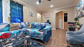 A living room with a sofa, a coffee table, and a chair. There is a ceiling fan and a door leading to another room.