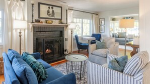 A living room with a fireplace, blue sofas, striped armchairs, and a small round table.