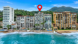 Ein Strandhotel mit mehreren Etagen, einem Poolbereich und Blick auf das Meer und die Berge.