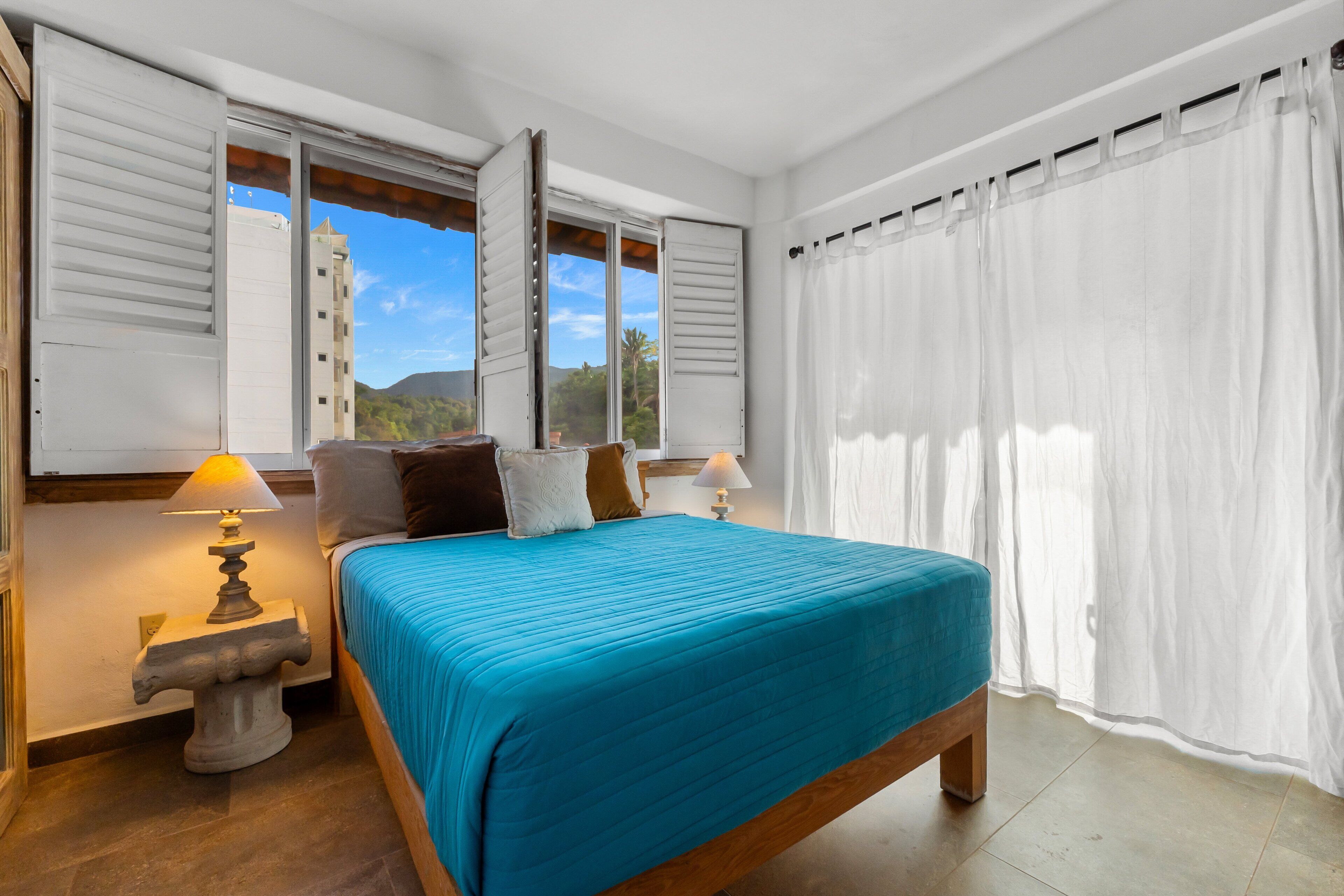 Una camera da letto con un letto, due lampade sui comodini, una finestra con persiane e vista sull'esterno.