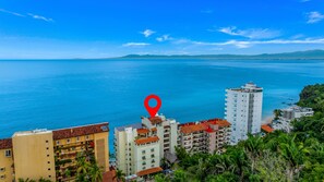 Un paysage urbain côtier avec de hauts immeubles, une mer bleue et limpide, et un marqueur de localisation rouge.
