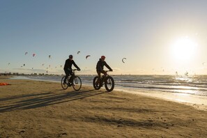 Ein Strand mit zwei Radfahrern und mehreren Drachen im Hintergrund.