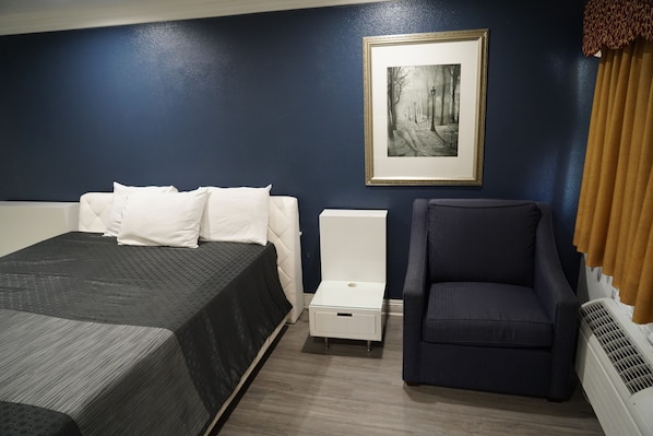 A hotel room with a bed, a chair, a small table, and a framed picture on the wall. - Flamingo Inn (Rosemead)