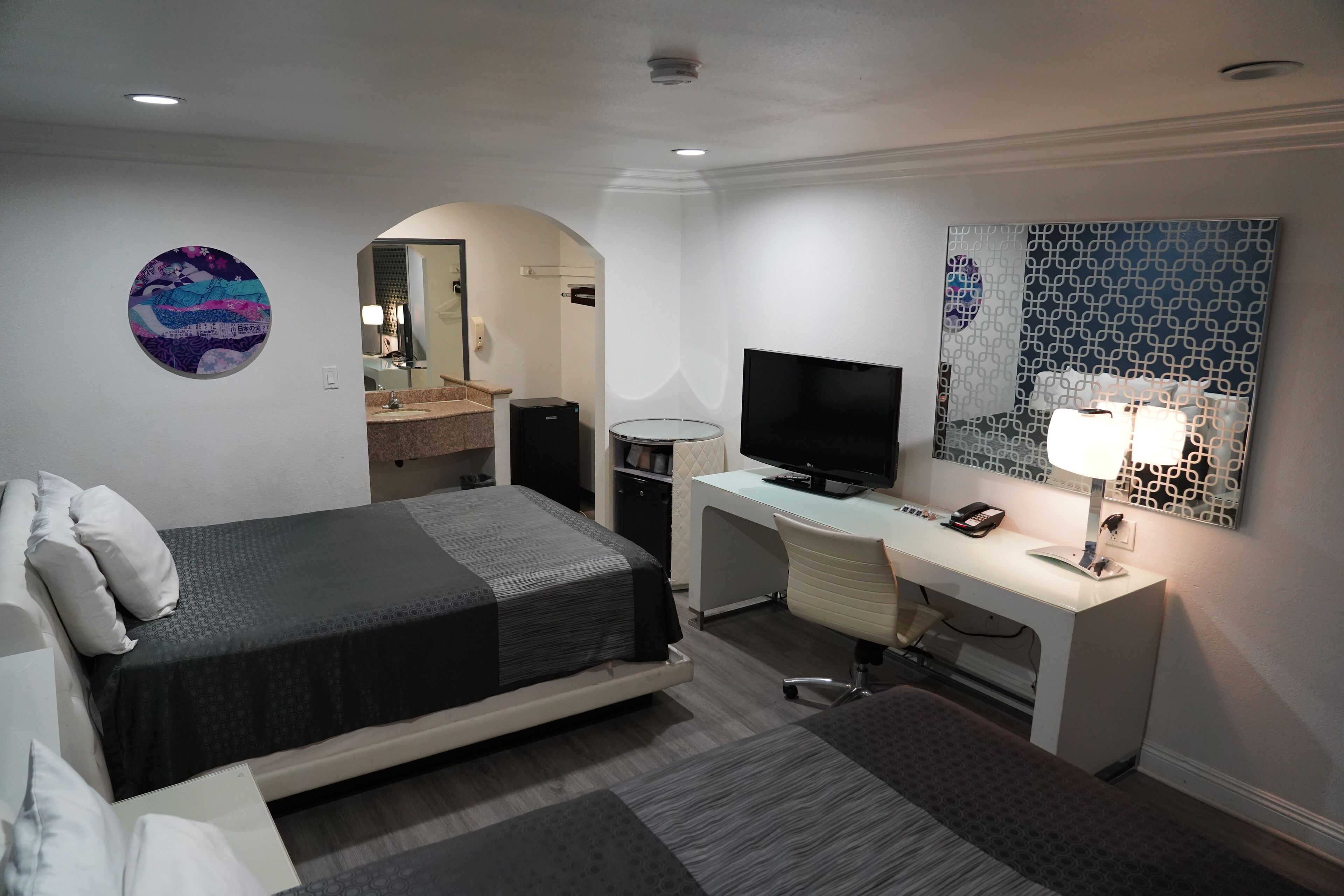 A modern hotel room with a bed, desk, television, and a bathroom visible through an archway.