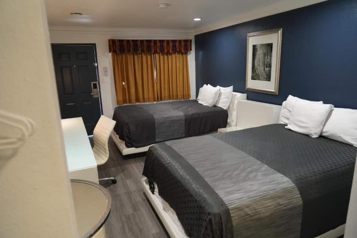 Ein Hotelzimmer mit zwei Betten, einer Tür, einem Fenster mit Vorhängen und einem gerahmten Bild an der Wand.