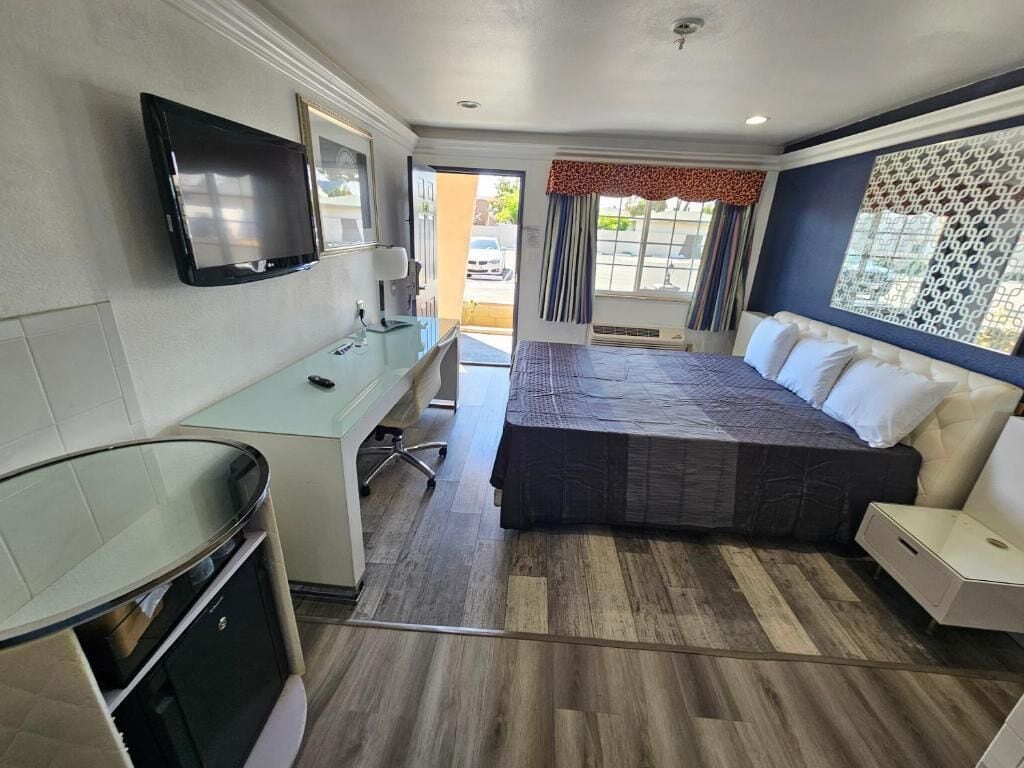 Quarto de hotel com cama, escrivaninha, televisão e janela com cortinas.
