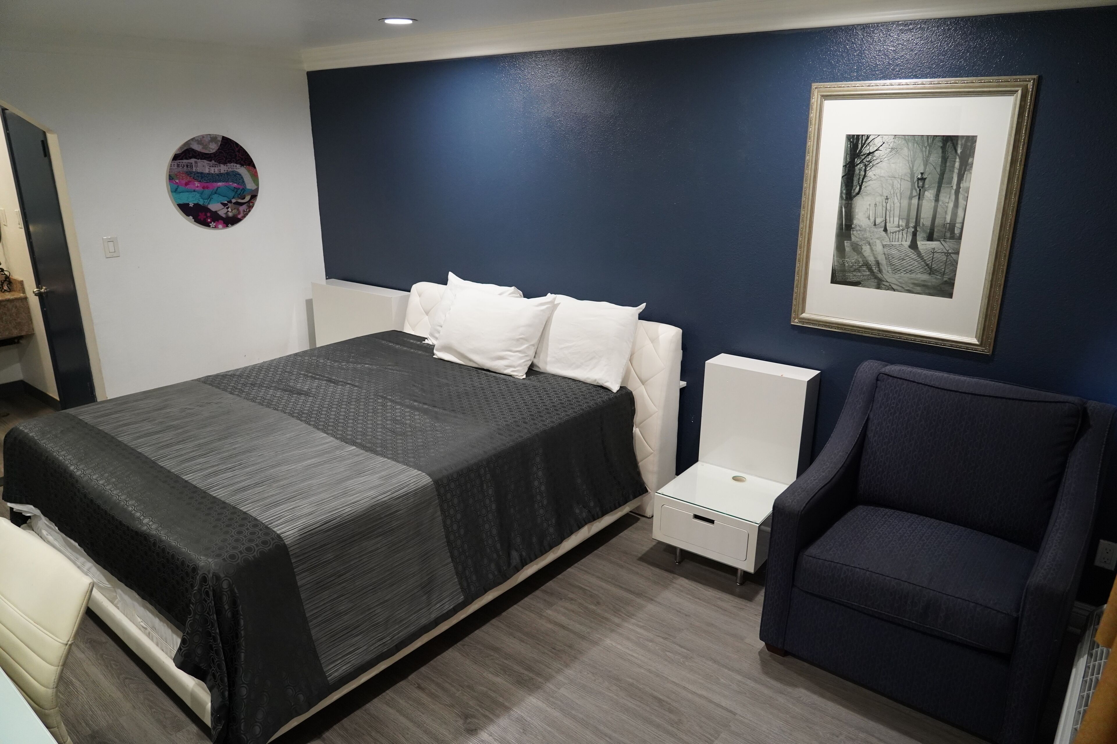 A bedroom with a bed, a chair, a bedside table, and a framed picture on the wall.
