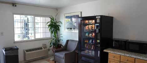 A compact kitchen with a refrigerator, microwave, and a small dining area with a chair and a potted plant.