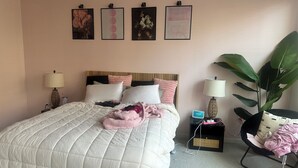 A neatly made bed with a white quilt, a bedside lamp, a clock, and a large plant. - 3-bedroom townhome in Atlanta near entertainment attractions (Atlanta)