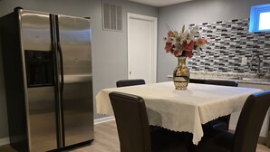 Une cuisine moderne avec un réfrigérateur en acier inoxydable, une table à manger avec des chaises et un vase décoratif avec des fleurs.