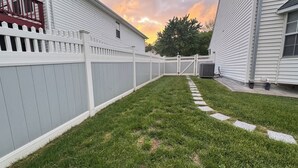 Un jardin avec une clôture blanche, une pelouse verdoyante et un chemin en pierre.