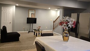 Un coin repas avec une table dressée pour deux personnes, un canapé noir, une petite table d’appoint agrémentée d’un objet décoratif et un escalier menant à un autre niveau.