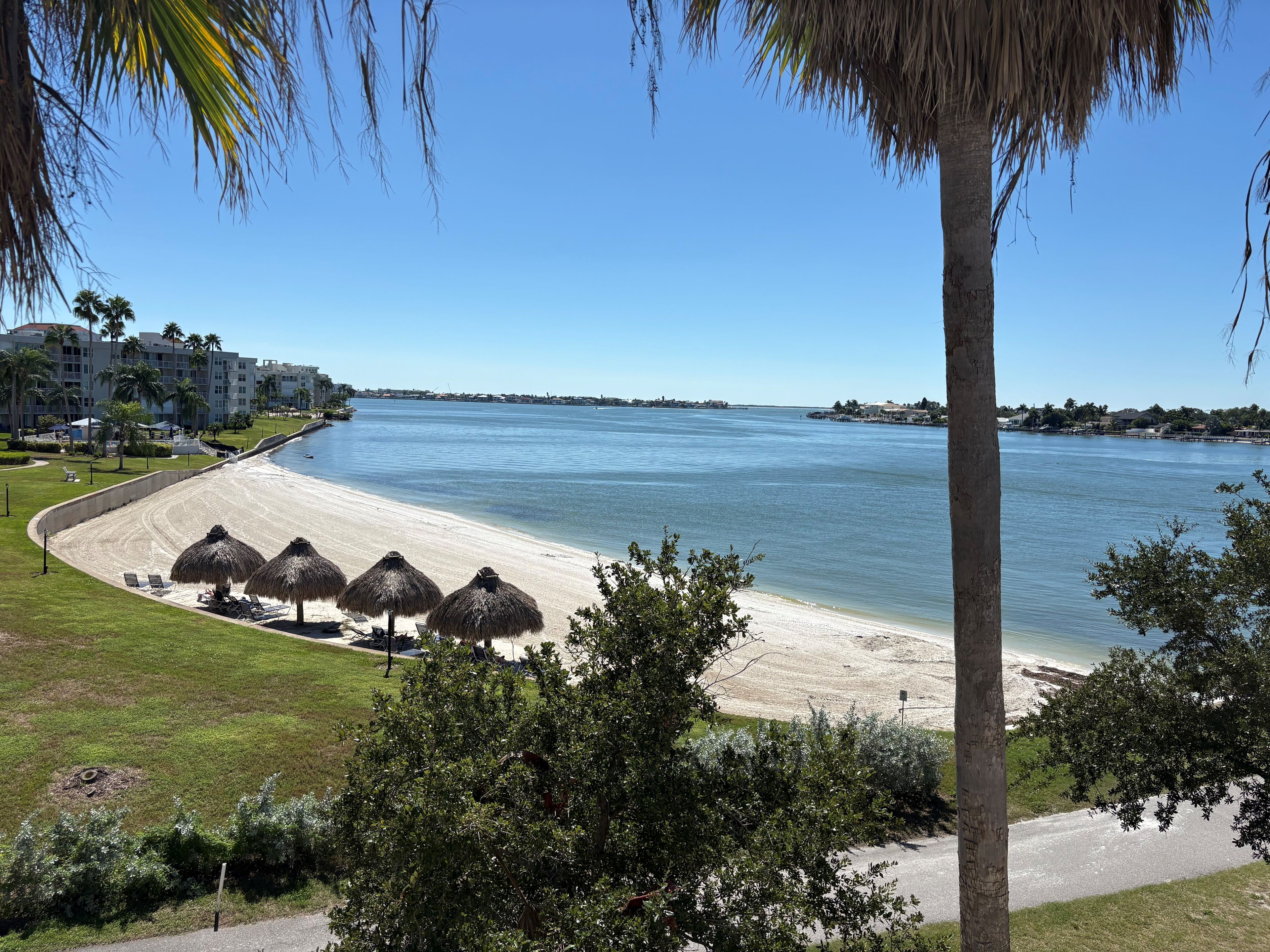 A beach with thatched umbrellas, a clear sky, and a view of the water.