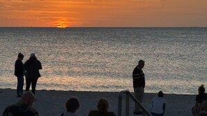 A sunset over the ocean with people standing on the beach. - A little slice of paradise in St Pete Beach (St. Petersburg)