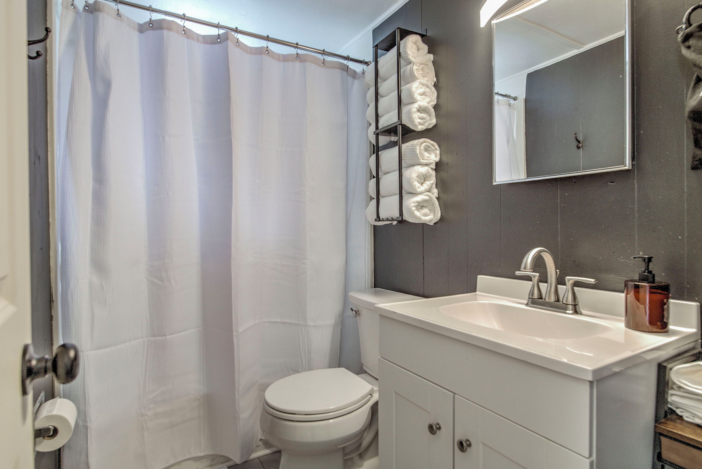 Un baño con cortina de ducha, inodoro, lavamanos con espejo y toallero.
