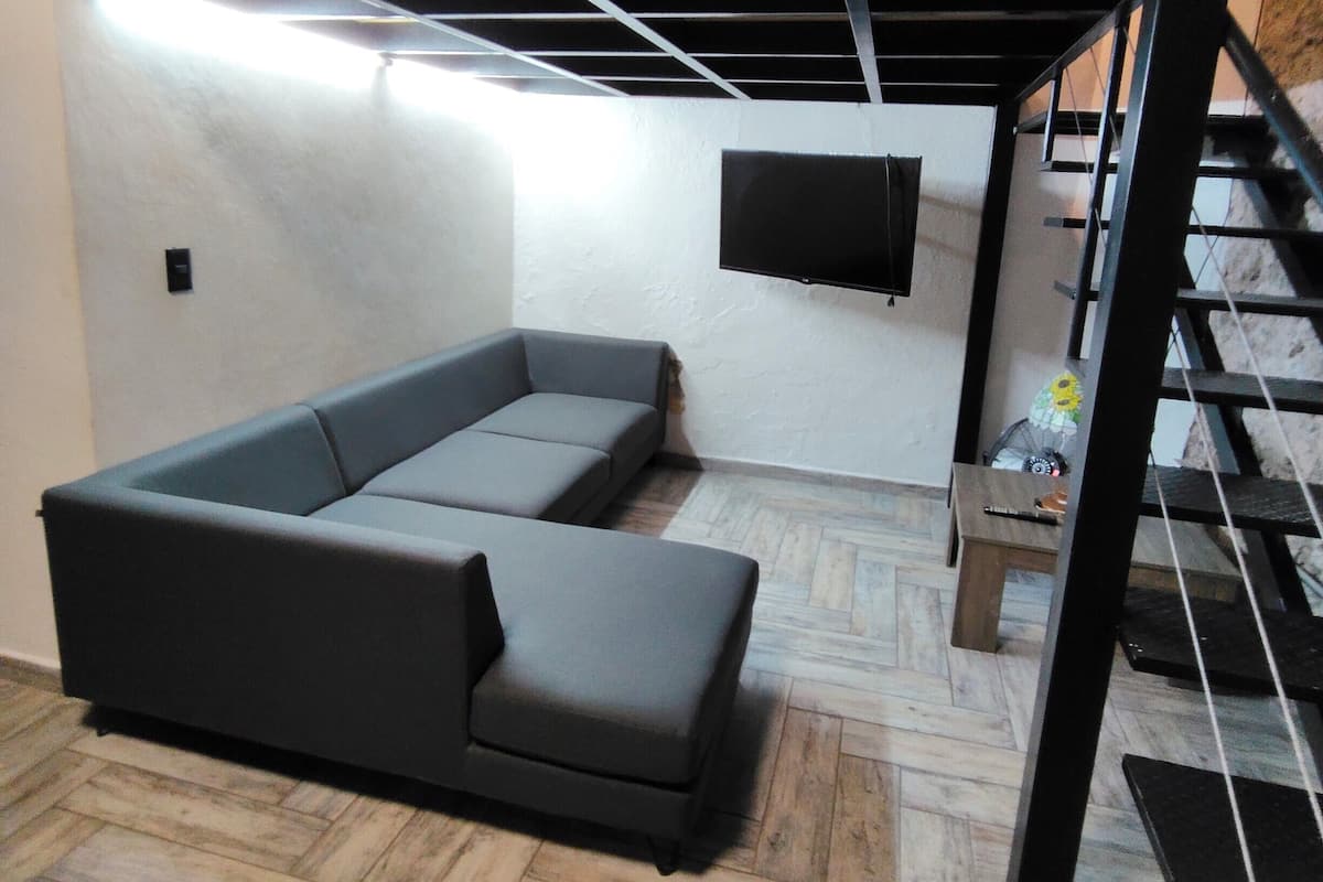 Ein modernes Wohnzimmer mit Ecksofa, einem flachbildfernseher an der Wand und einem Holzboden mit Fischgrätmuster.