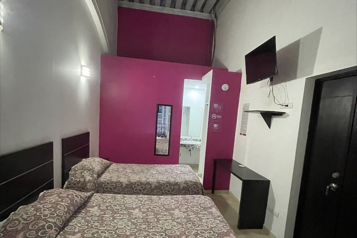 Ein Schlafzimmer mit zwei Betten, einem Fernseher, einer Tür und einem Fenster.