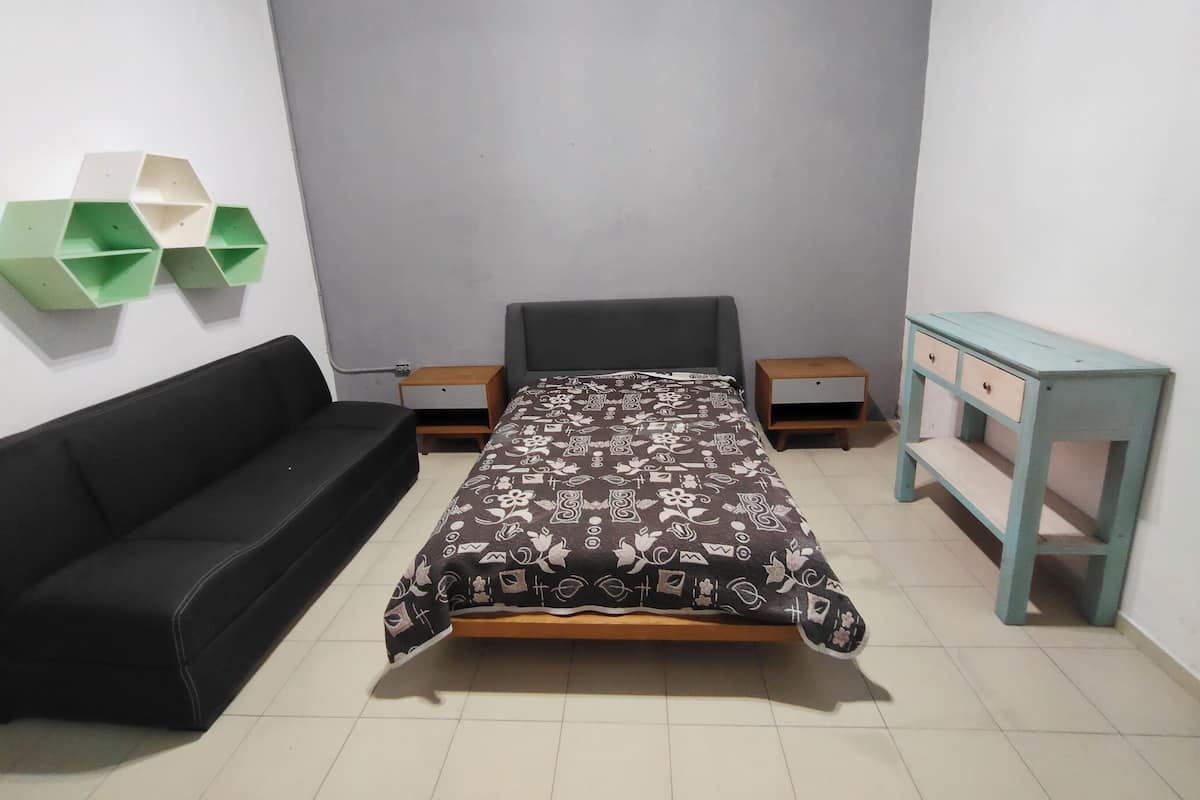 Ein Schlafzimmer mit einem Bett, einer schwarzen Couch, zwei Nachttischen, einer Kommode und grünen Regallkästen an der Wand.
