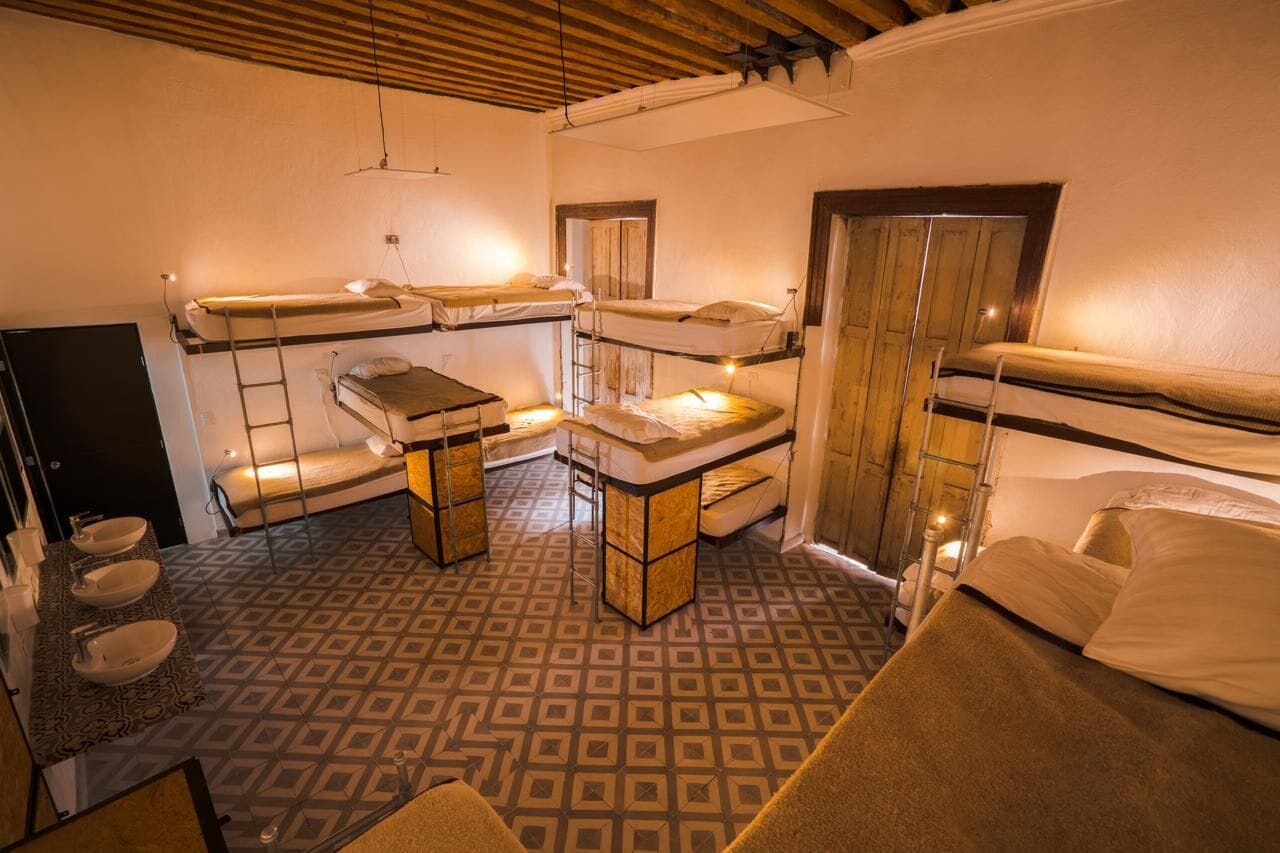 Habitación tipo dormitorio con literas, un escritorio pequeño y un baño con tres lavamanos.