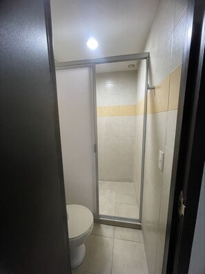 Pieni, suljettu suihkutila, jossa on wc, laatoitetut seinät ja kattovalaisin.