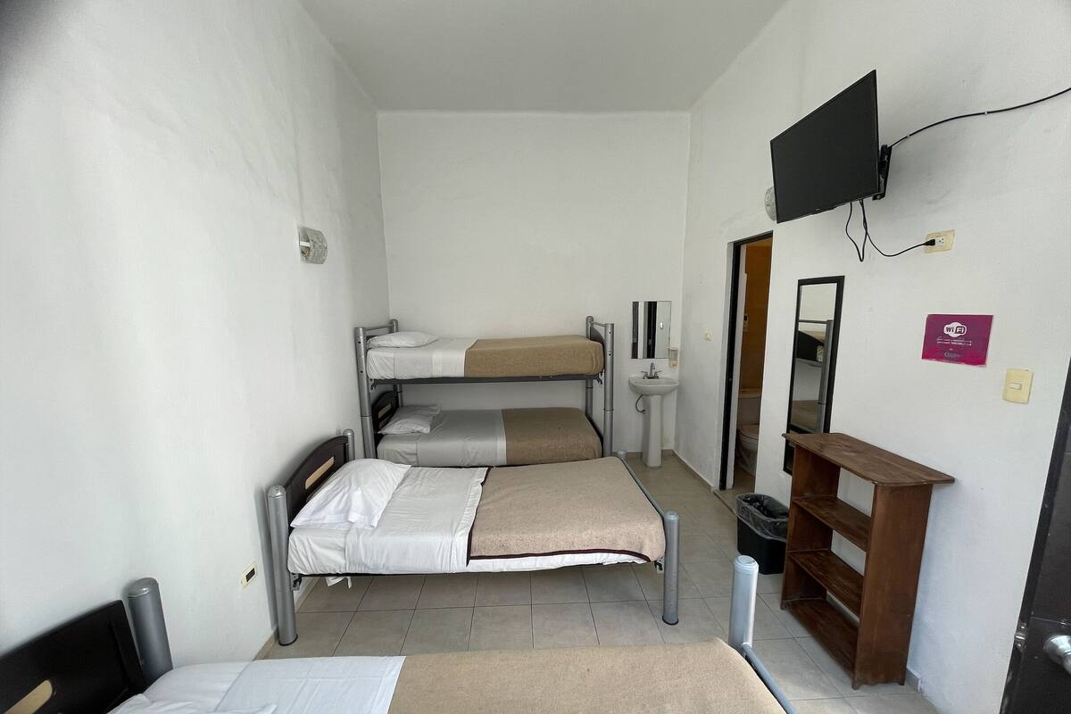 Ein kleines Zimmer mit Etagenbetten, einem Waschbecken, einem Spiegel, einem Fernseher und einer Holzbank.
