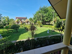 A well-maintained garden with neatly trimmed hedges and a variety of trees, leading to a building with a yellow facade and red roof. - Rim Khao Resort (Ko Lanta)