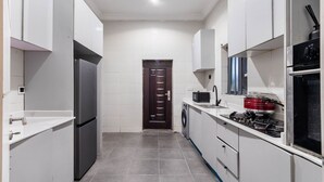 Eine kleine Küche mit weißen Schränken, einem Kühlschrank, einer Mikrowelle, einem Herd und einer Waschmaschine.