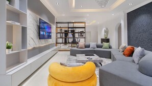Ein modernes Wohnzimmer mit grauem Sofa, gelbem Sitzsack und einem an der Wand befestigten Fernseher.