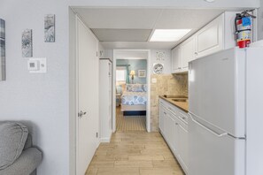A narrow hallway leading to a bedroom with a bed, a bathroom with a sink, and a kitchen with a refrigerator.