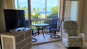 Una habitación con televisión sobre un mueble de madera, una mesa de comedor con sillas y vista al océano a través de ventanas amplias.