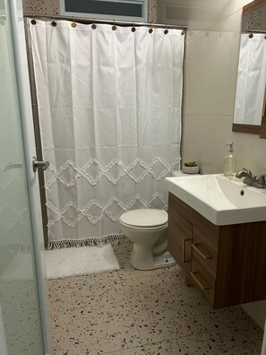 Et badeværelse med bruseforhæng, toilet, håndvask og spejl.