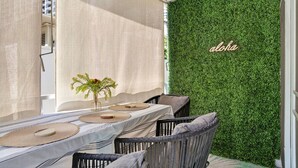 Un comedor con una mesa preparada para dos personas, una pared verde con la palabra 'aloha' escrita y una vista de un edificio al fondo.