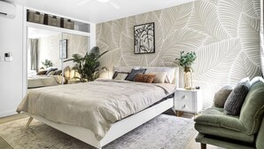Un dormitorio con cama, mesita de noche, sillón verde y un espejo grande.