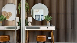 Un baño moderno con un tocador de madera, dos espejos, un lavabo redondo y un taburete pequeño.