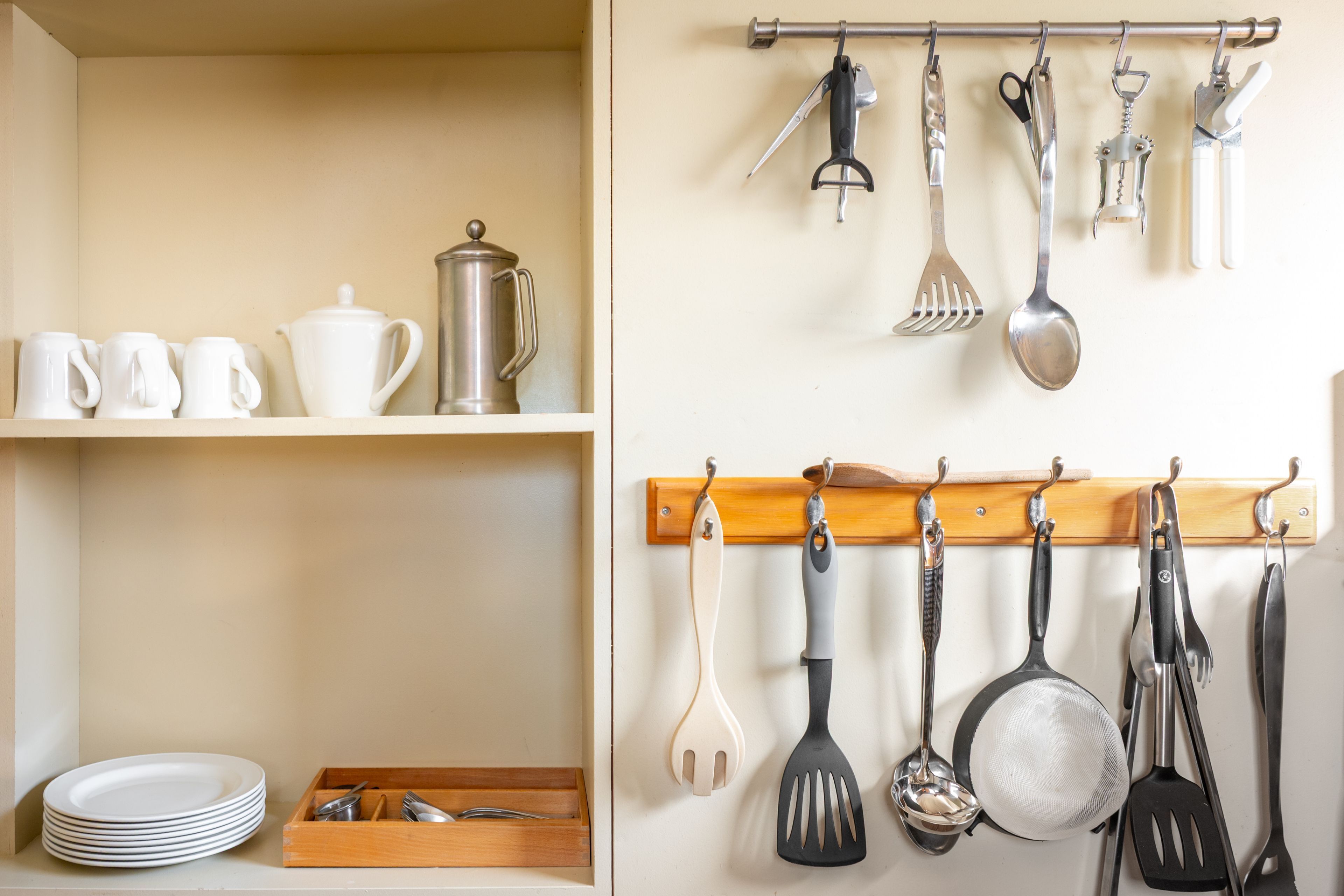 A kitchen with white plates, a teapot, and utensils on shelves and hanging on hooks.