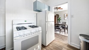 A modern kitchen with white appliances, a blue cabinet, and a dining area with a wooden table and chairs. - Serene Suburban Stay: Family-Friendly w/EZ Parking (Berwyn)