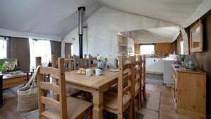 Un hébergement sous tente comprenant un espace repas avec des meubles en bois, une cuisine et un coin salon confortable.
