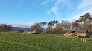 Eine ländliche Landschaft mit einem großen, offenen Feld, mehreren Holzbauten und einem klaren Himmel.