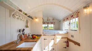 Une cuisine compacte dotée d’un plan de travail en bois, de meubles blancs et d’une fenêtre donnant sur un espace verdoyant.