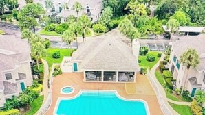 Una zona residencial con piscina rodeada por una terraza de madera, abundante vegetación y casas.
