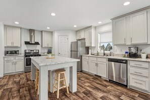 A modern kitchen with white cabinets, stainless steel appliances, and a wooden floor. - Views for MILES ~ Remote Home in the Ranch (Butte)
