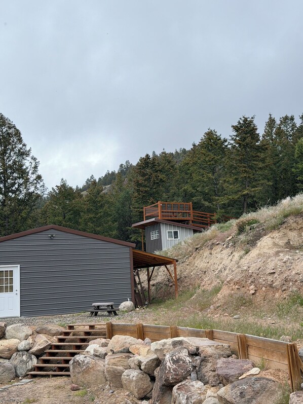 A rustic cabin with a metal exterior, a wooden deck, and a stone staircase leading to a raised platform. - The Aspens are Golden NOW- Remote Home w/ Views (Butte)