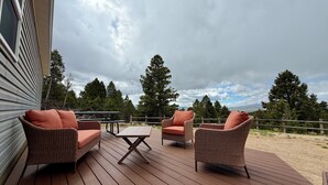Eine Holzterrasse mit Korbmöbeln und einem Tisch, mit Blick auf eine bewaldete Landschaft.