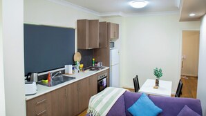 Eine kleine Küche mit Spüle, Herd und Schränken, ein Esstisch mit Stühlen und ein violettes Sofa mit gestreifter Decke.